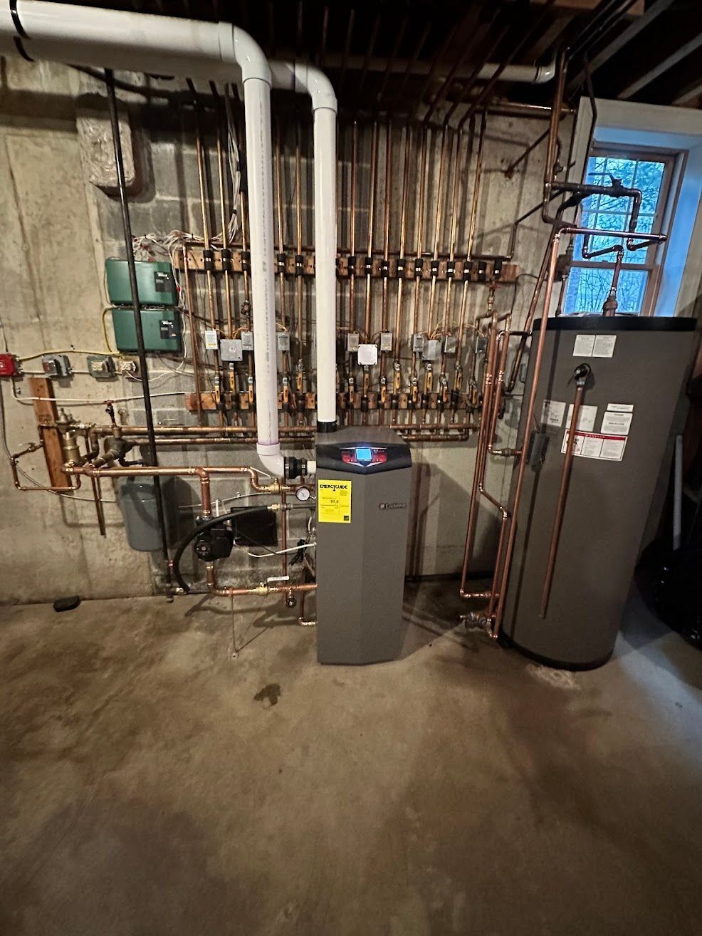 A gas boiler is sitting in a basement next to a water heater.