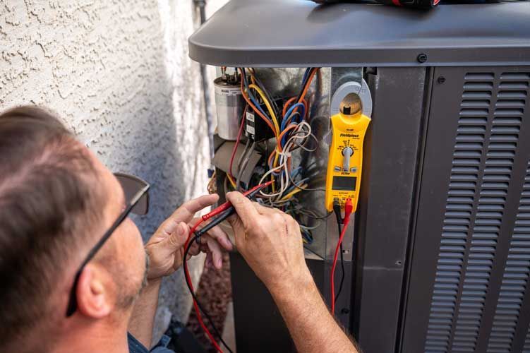 A man is working on an air conditioner with a voltmeter.