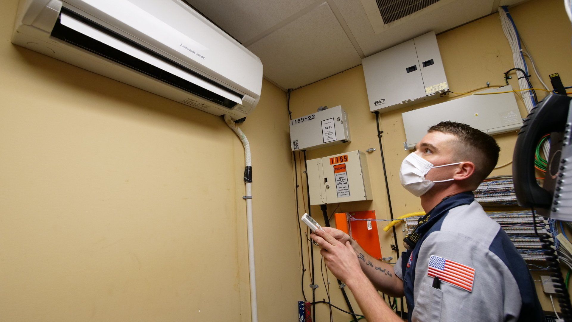 A man wearing a mask is working on an air conditioner in a room.
