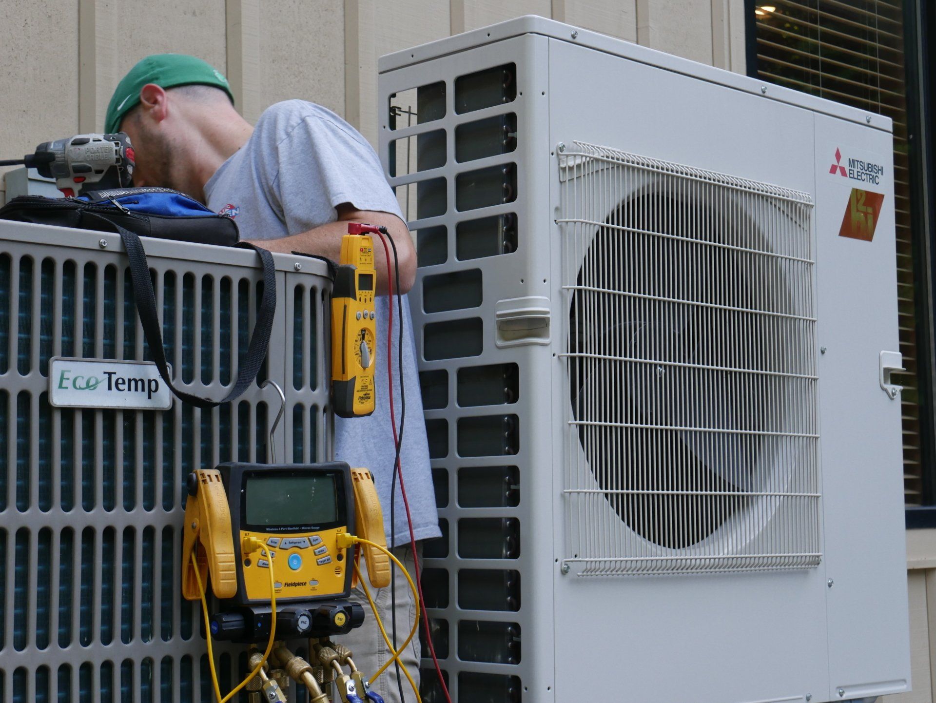 A man is working on an air conditioner outside of a building.