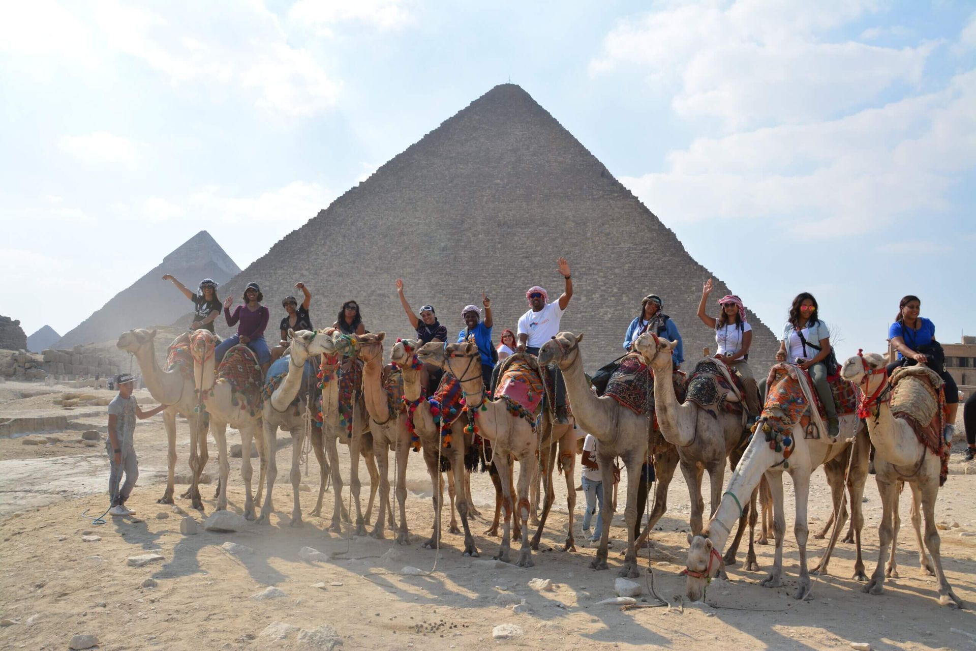 A group of people riding camels in front of two pyramids.