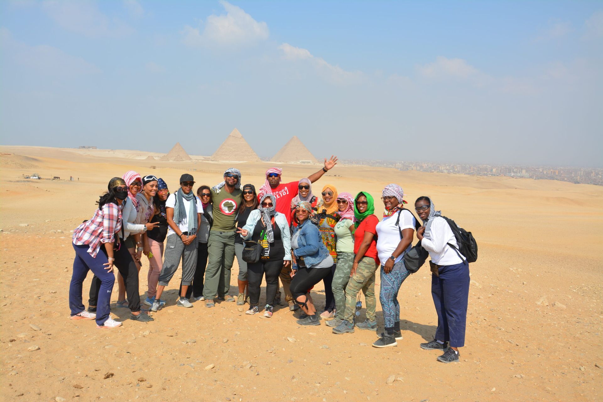 A group of people are posing for a picture in the desert in front of the pyramids.