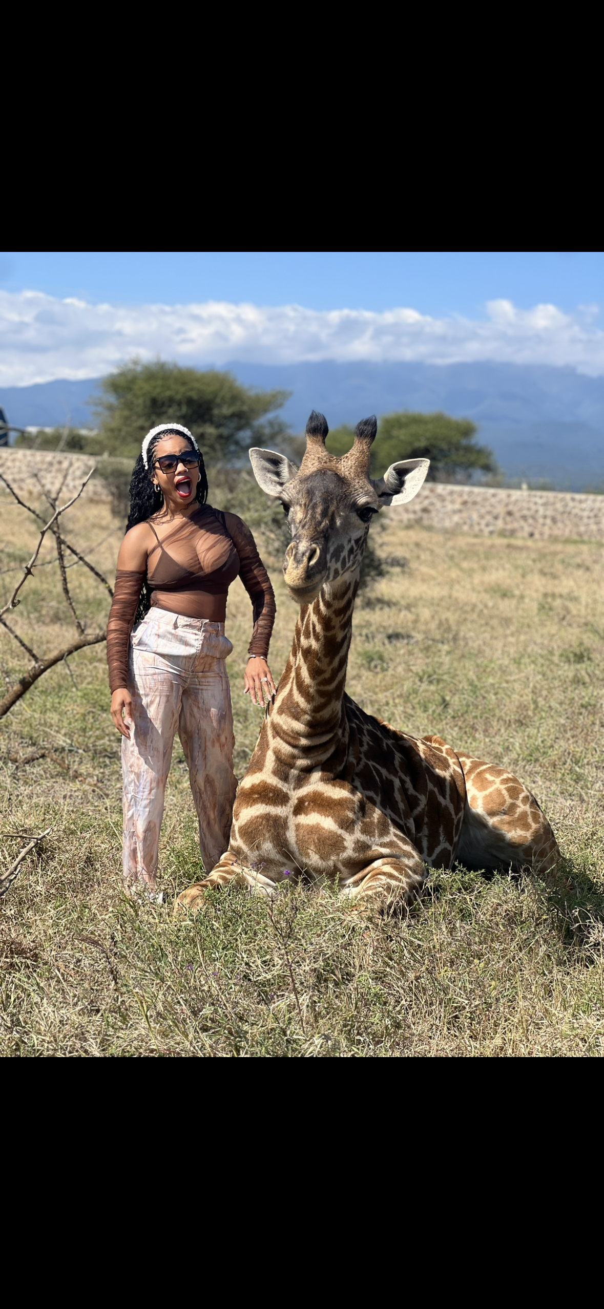 A woman is standing next to a giraffe in a field.