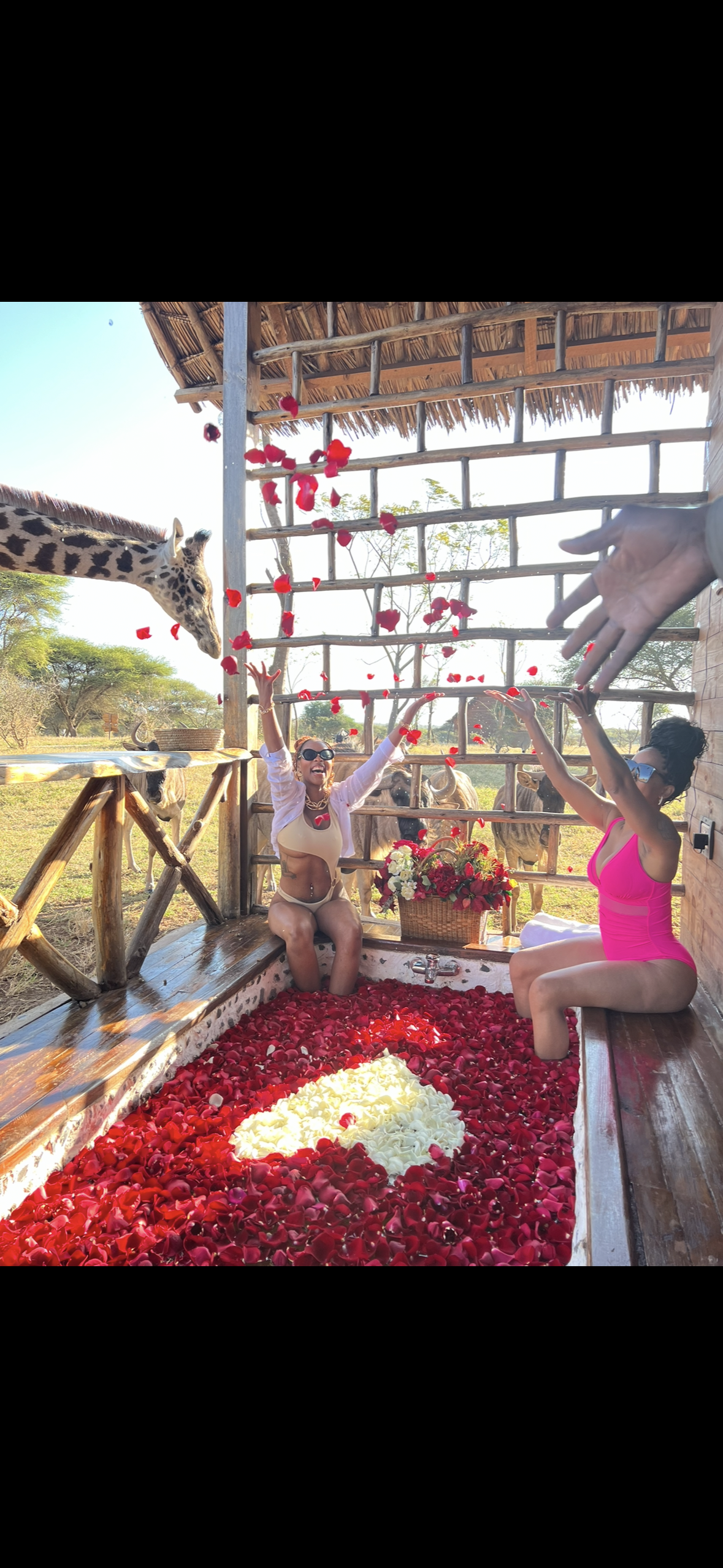 Two women are sitting in a bathtub filled with rose petals.