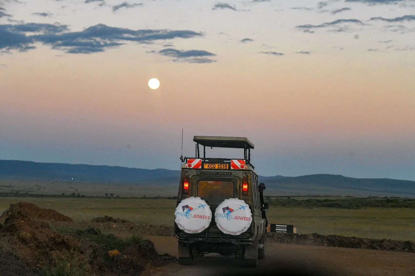 A jeep is driving down a dirt road at sunset.