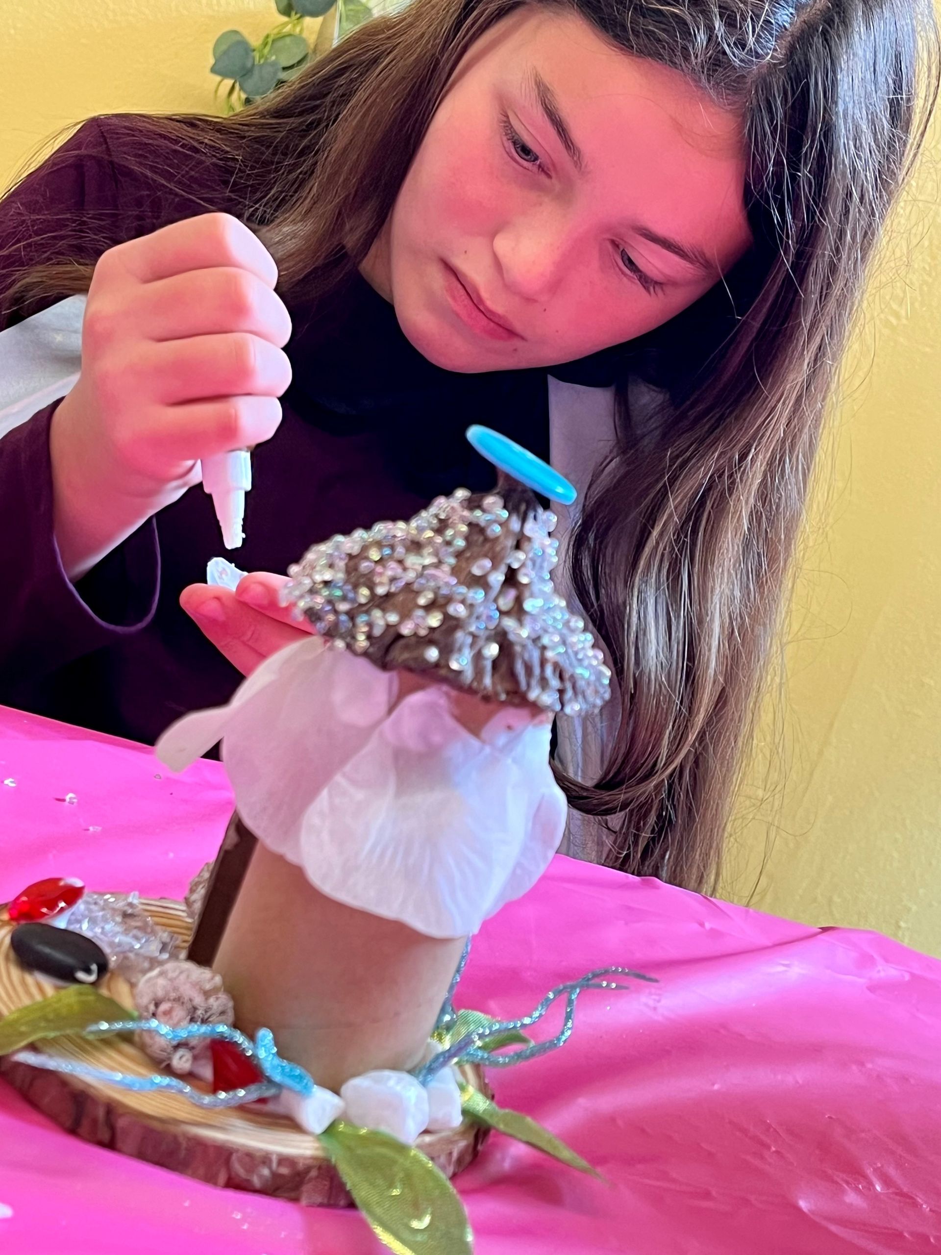 A girl is sitting at a table decorating a fairy house
