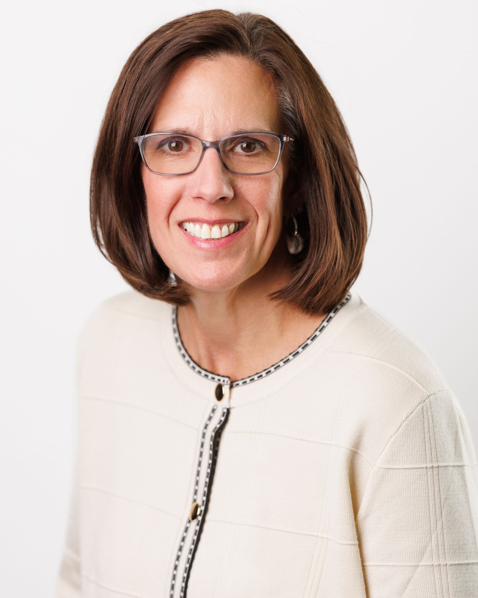 Woman with glasses, smiling, wearing a cream-colored sweater with black trim.