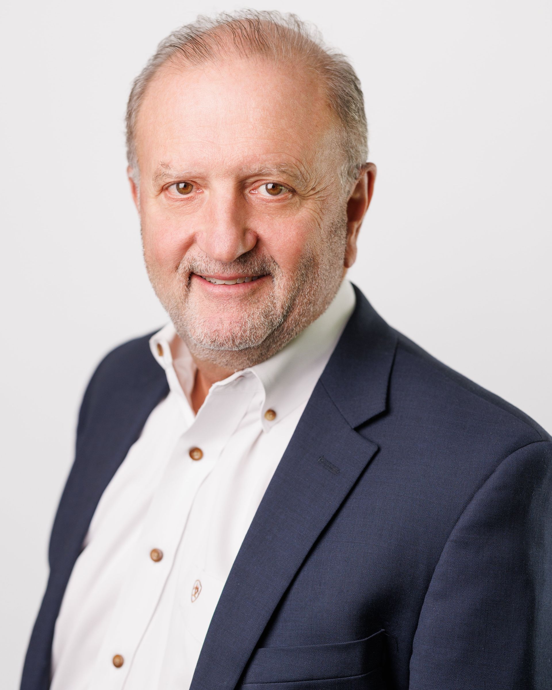 Man in navy blazer and white shirt smiles, head and shoulders portrait.