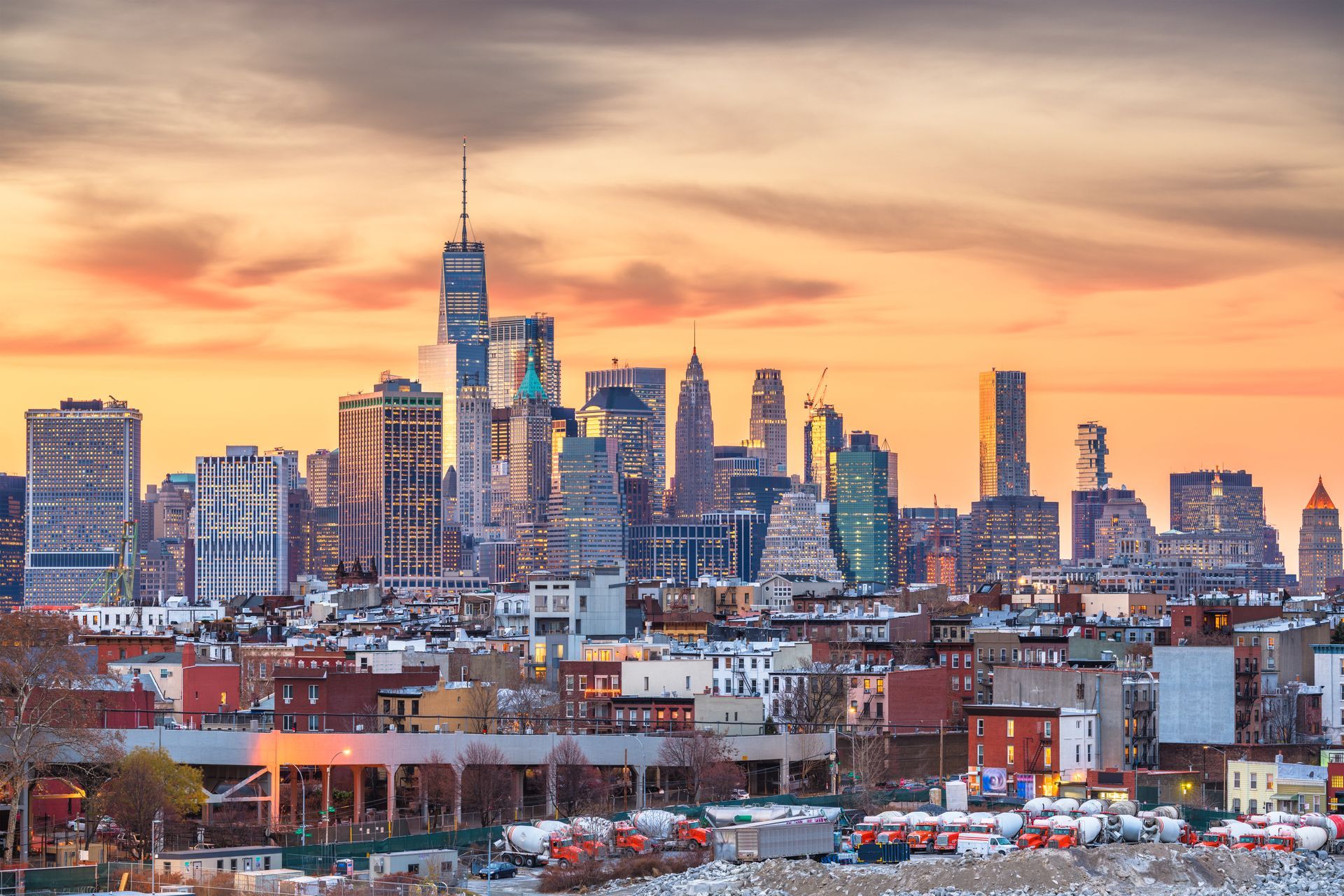 New York City skyline at sunset with orange and yellow sky over buildings.