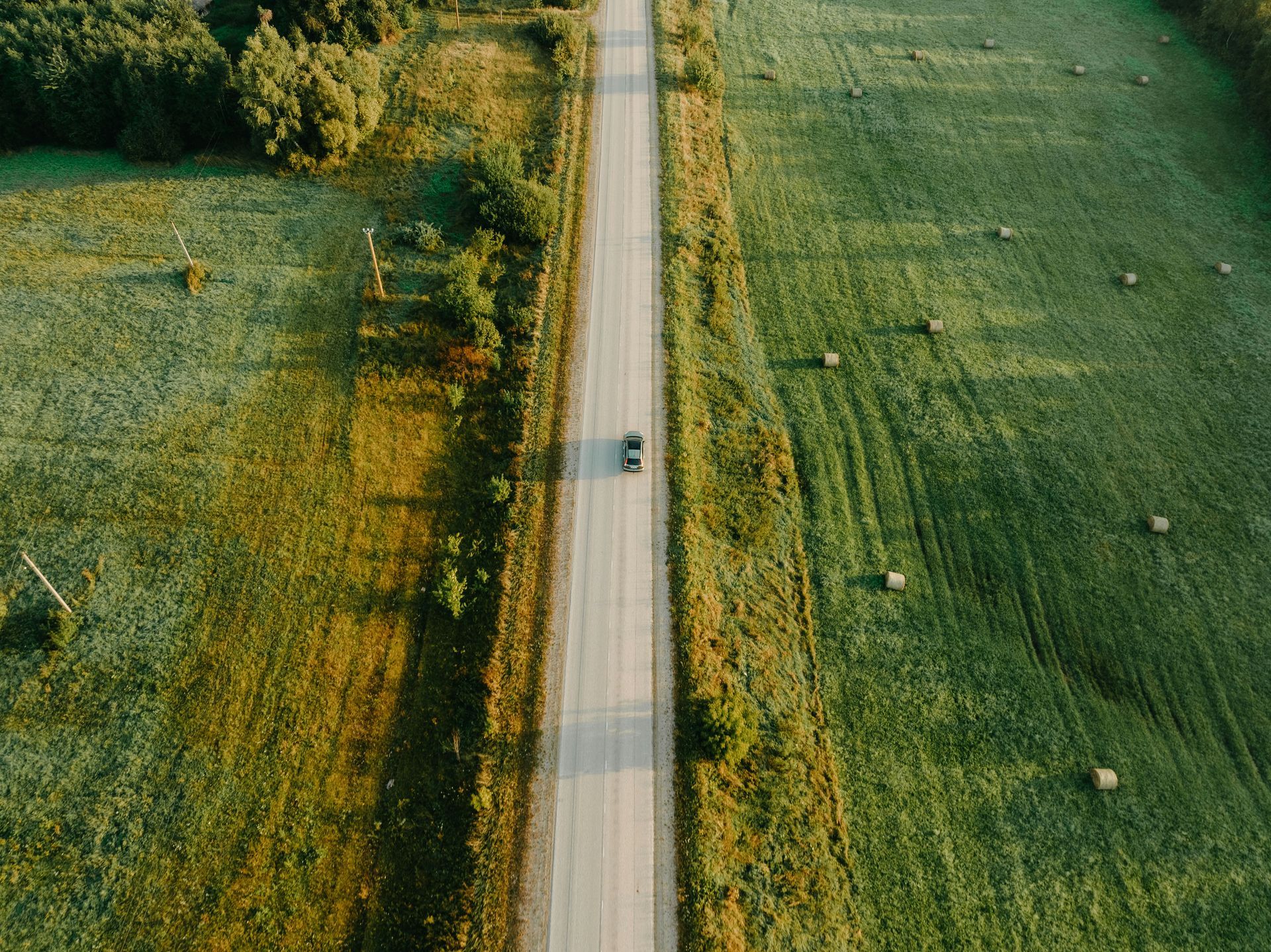 Aerial view of a car on a road, flanked by green fields.