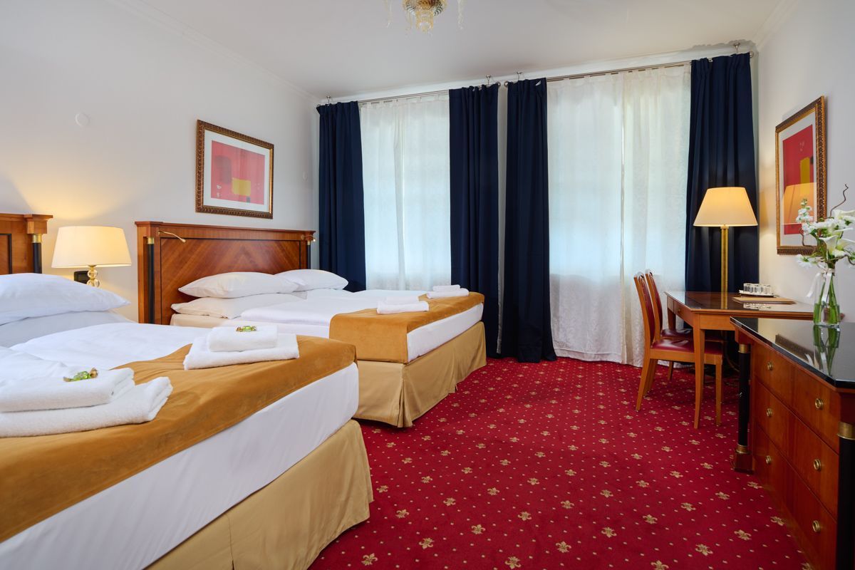 Hotel room with two twin beds, desk, and red carpet.