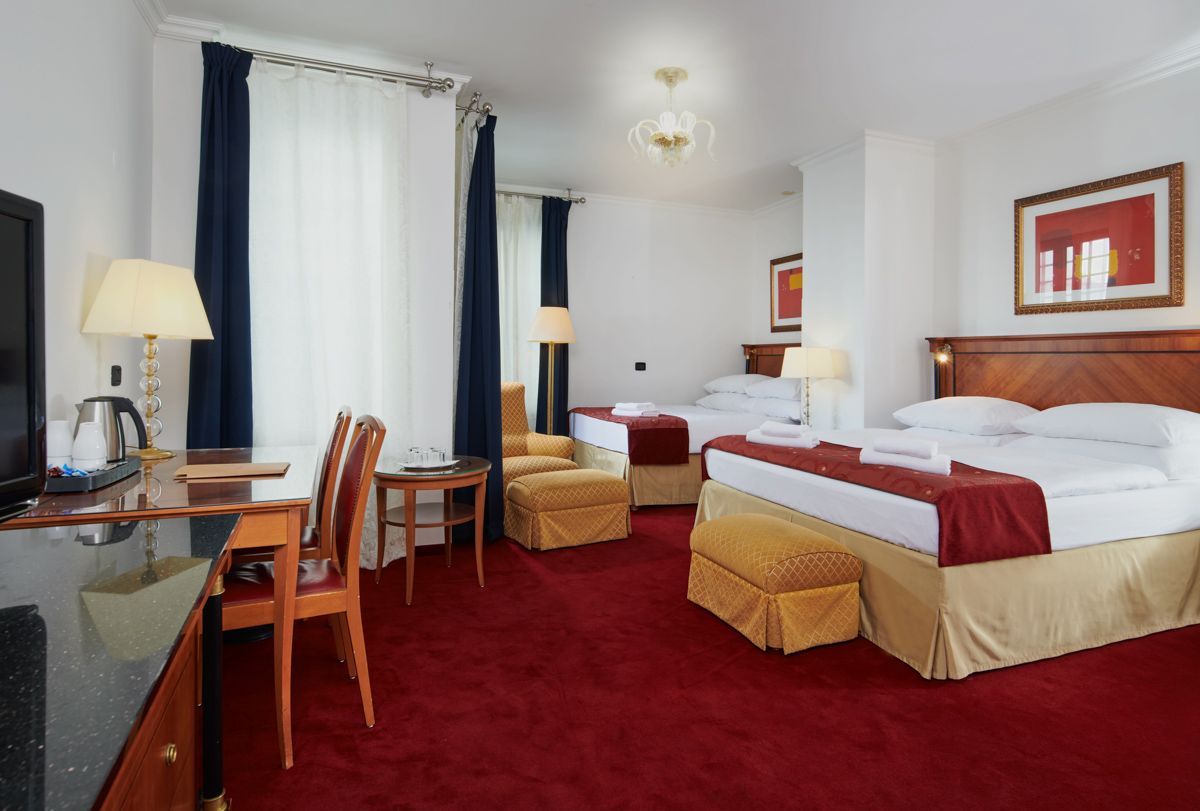 Hotel room with two double beds, red carpet, desk, and window with curtains.