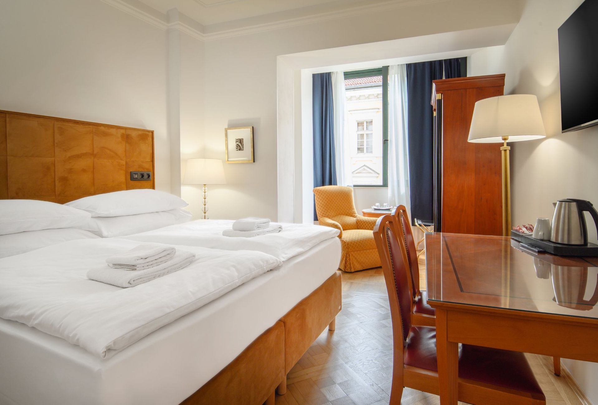 Hotel room with a double bed, desk, armchair, and window. Bright, clean room, warm colors.