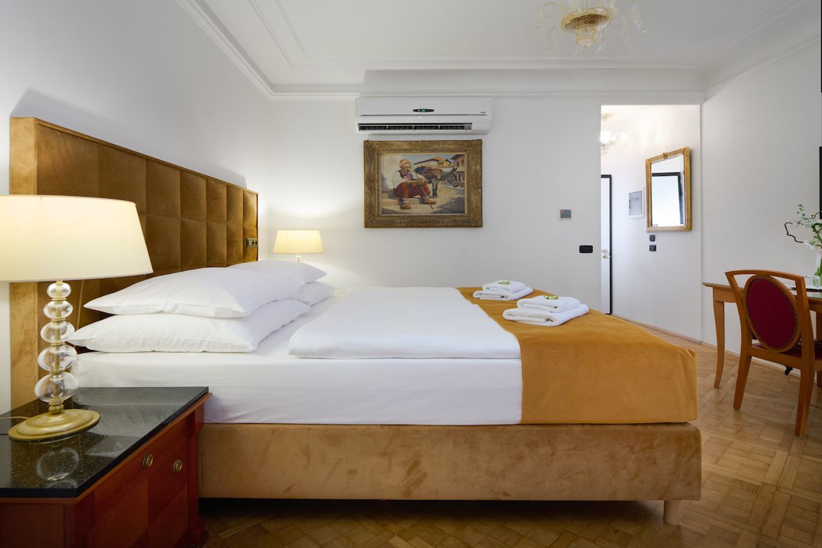 Bedroom with a bed, nightstand with lamp, and a desk. Gold and white color scheme.