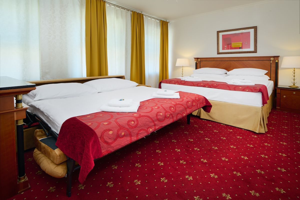 Hotel room with a double bed, a pull-out bed, red carpet, and yellow curtains.