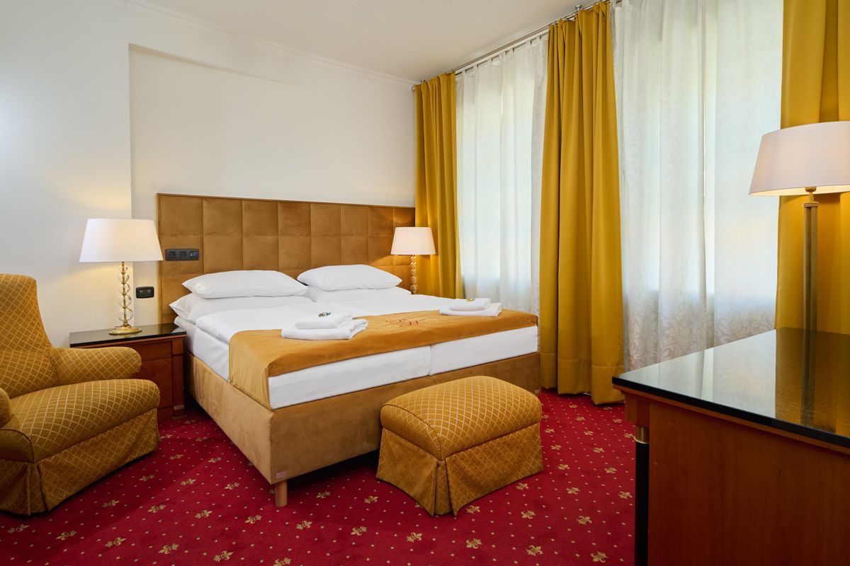 Hotel bedroom with a double bed, yellow curtains, red carpet, and a matching armchair.
