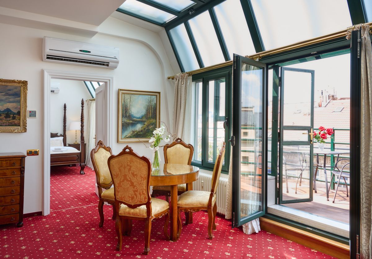 Hotel suite with red carpet, table and chairs, and balcony.