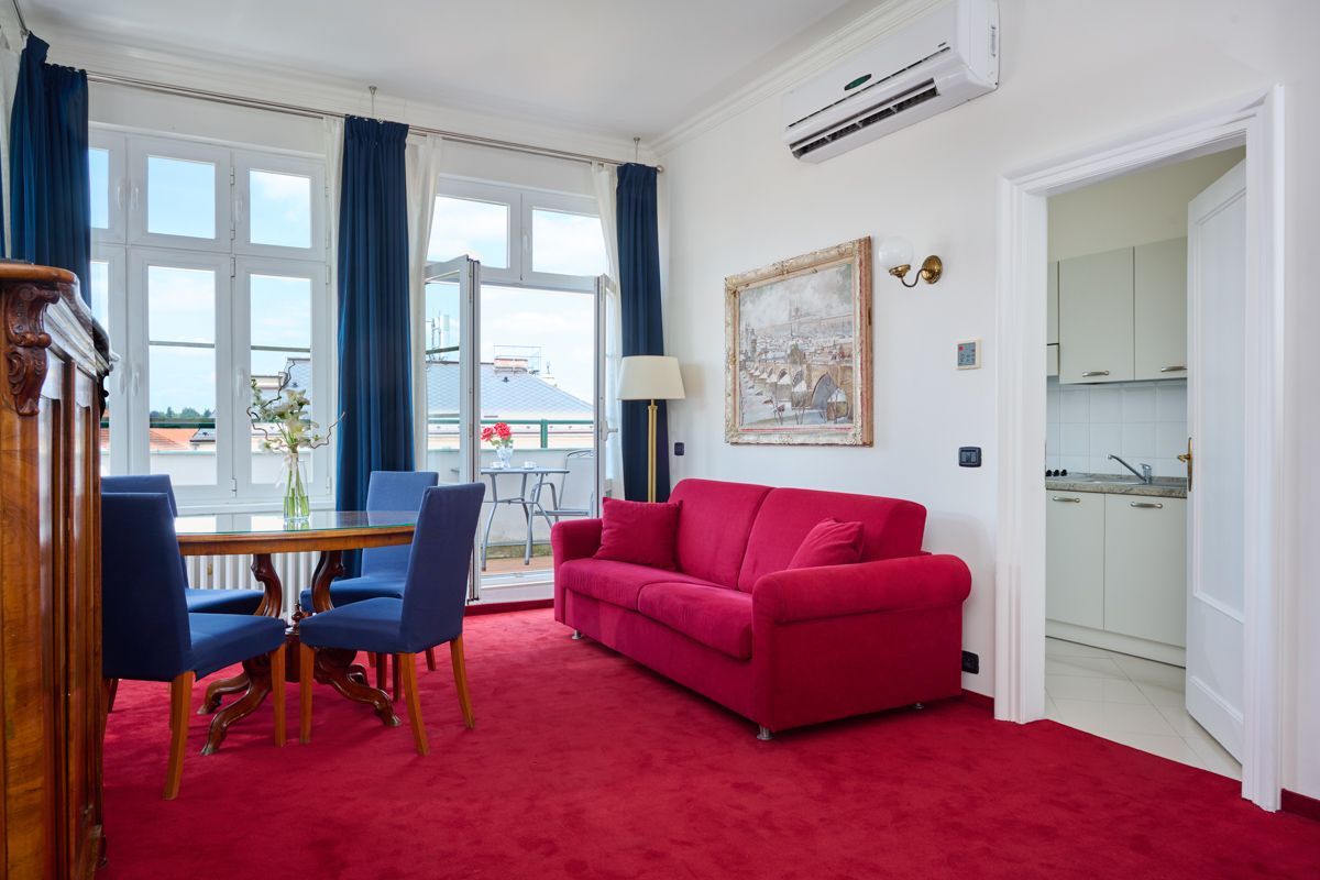 Living room with red carpet, red sofa, blue chairs, and an open doorway to a small kitchen.