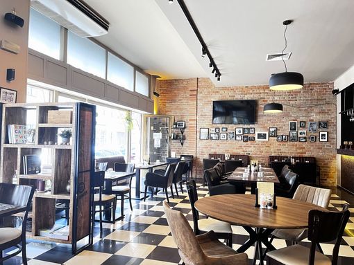 Restaurant interior with brick wall, checkered floor, tables, chairs, and a bookshelf.
