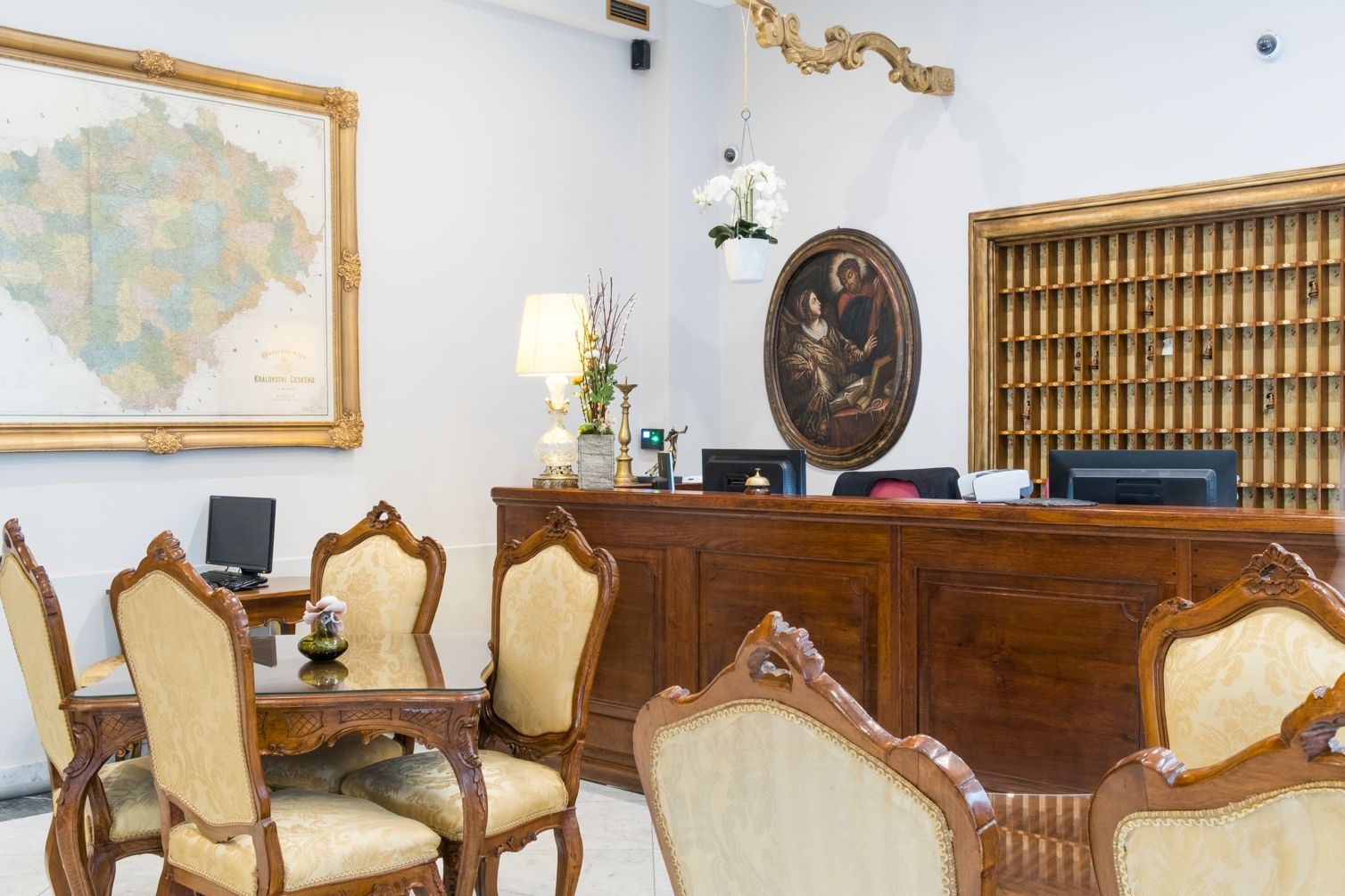 Hotel lobby with antique furniture, reception desk, framed map, and artwork.