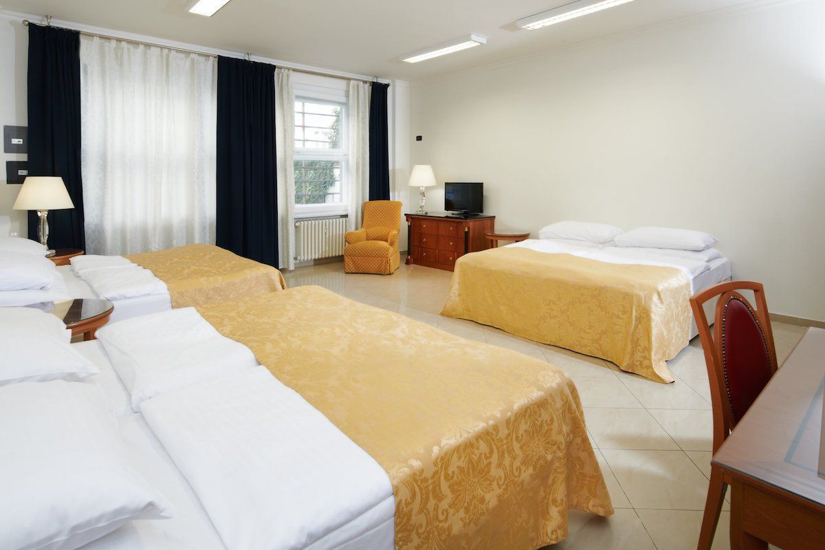 A hotel room with four beds covered in yellow bedspreads, a chair, TV, and a desk by a window.