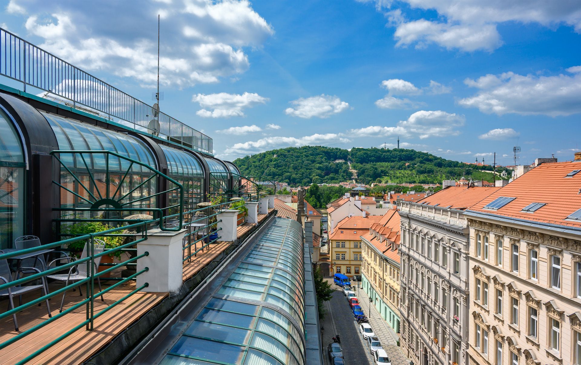 Rooftop view of European city with buildings, blue sky, and a distant hill.