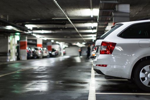 White car parked in an underground parking garage. Dark, wet pavement, other cars, and people are in the background.