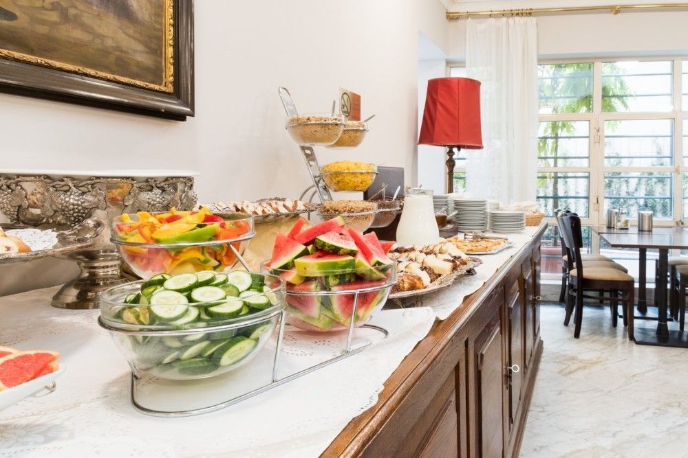 Breakfast buffet with fruits, pastries, and a lamp in a bright room.