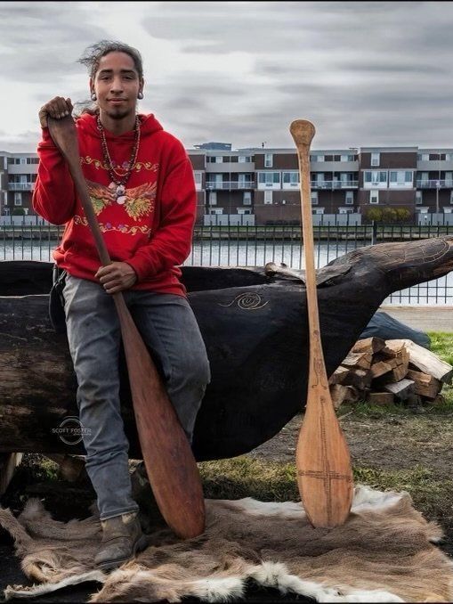 Daishuan Tallhairreddeer Garate leaning on a mishoon, holding a paddle.