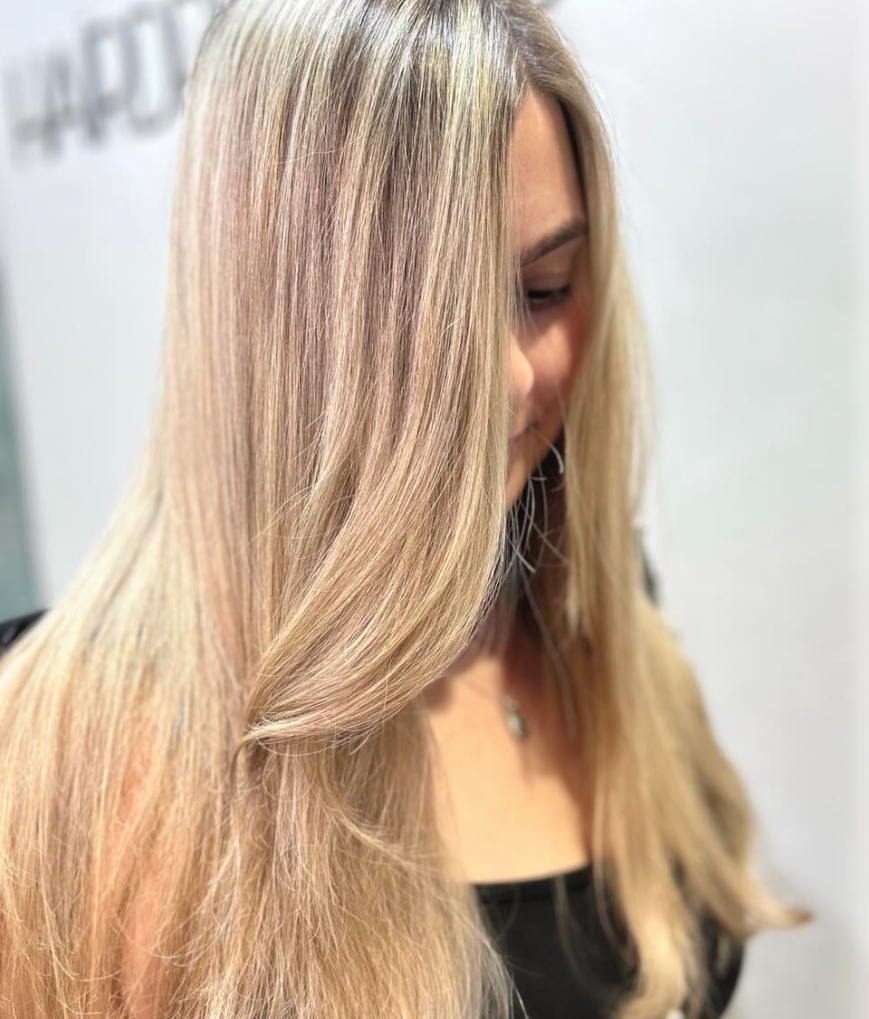 A Woman With Long Blonde Hair is Wearing a White Tank Top — Hairdresser At Work in Cairns City, QLD