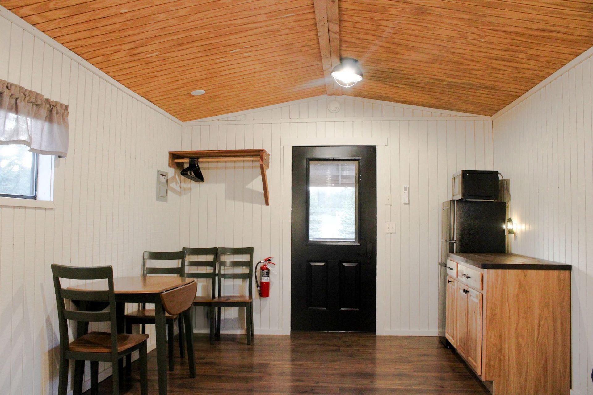 Small dining area with wood ceiling, table and chairs, black door, and cabinet with kettle.