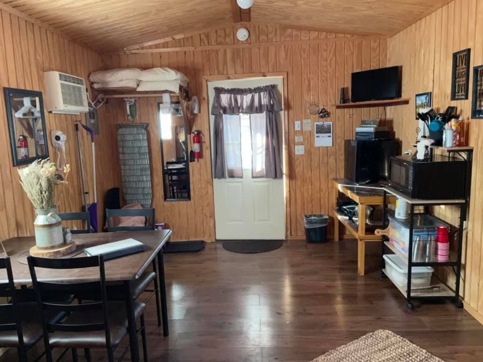 Cozy cabin interior with wood paneling, dark wood table, chairs, TV, and microwave.