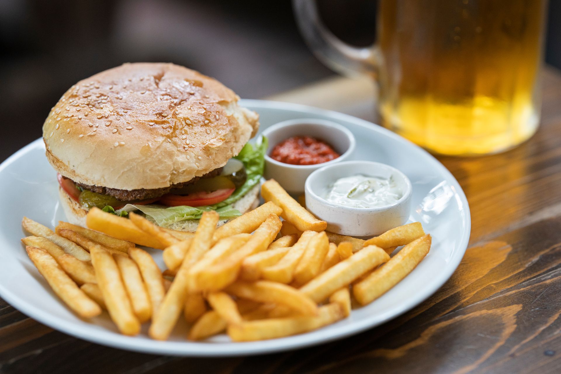 Burger, fries, and dipping sauces on a plate with a beer mug in the background.