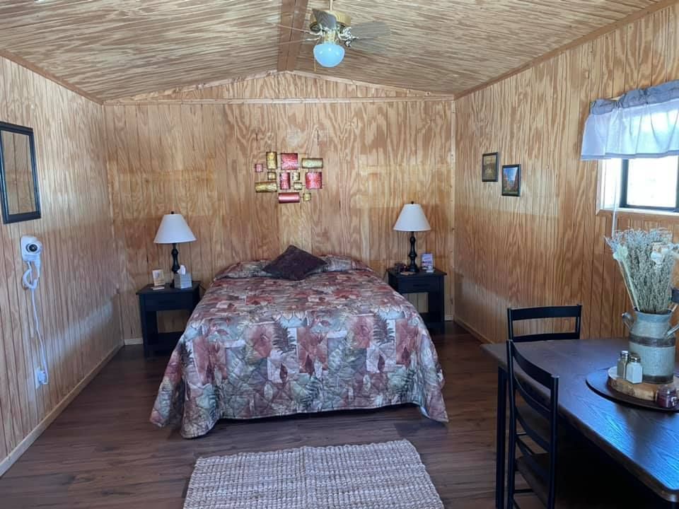 Bedroom interior with wood panel walls, bed, nightstands, lamps, small table, rug, and dried flowers.