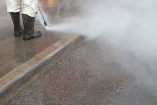 A man is cleaning graffiti on a blue garage door with a high pressure washer.