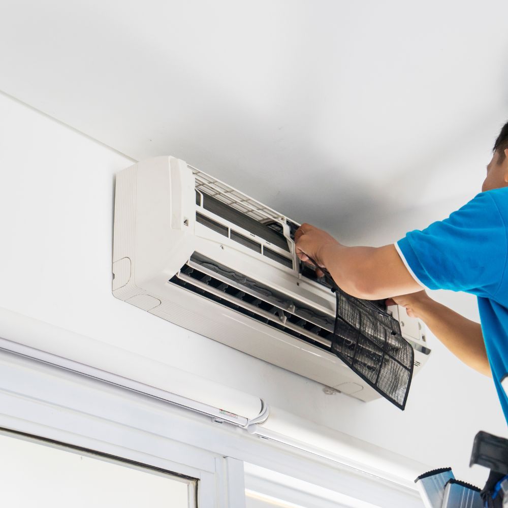 A man in a blue shirt is working on an air conditioner.