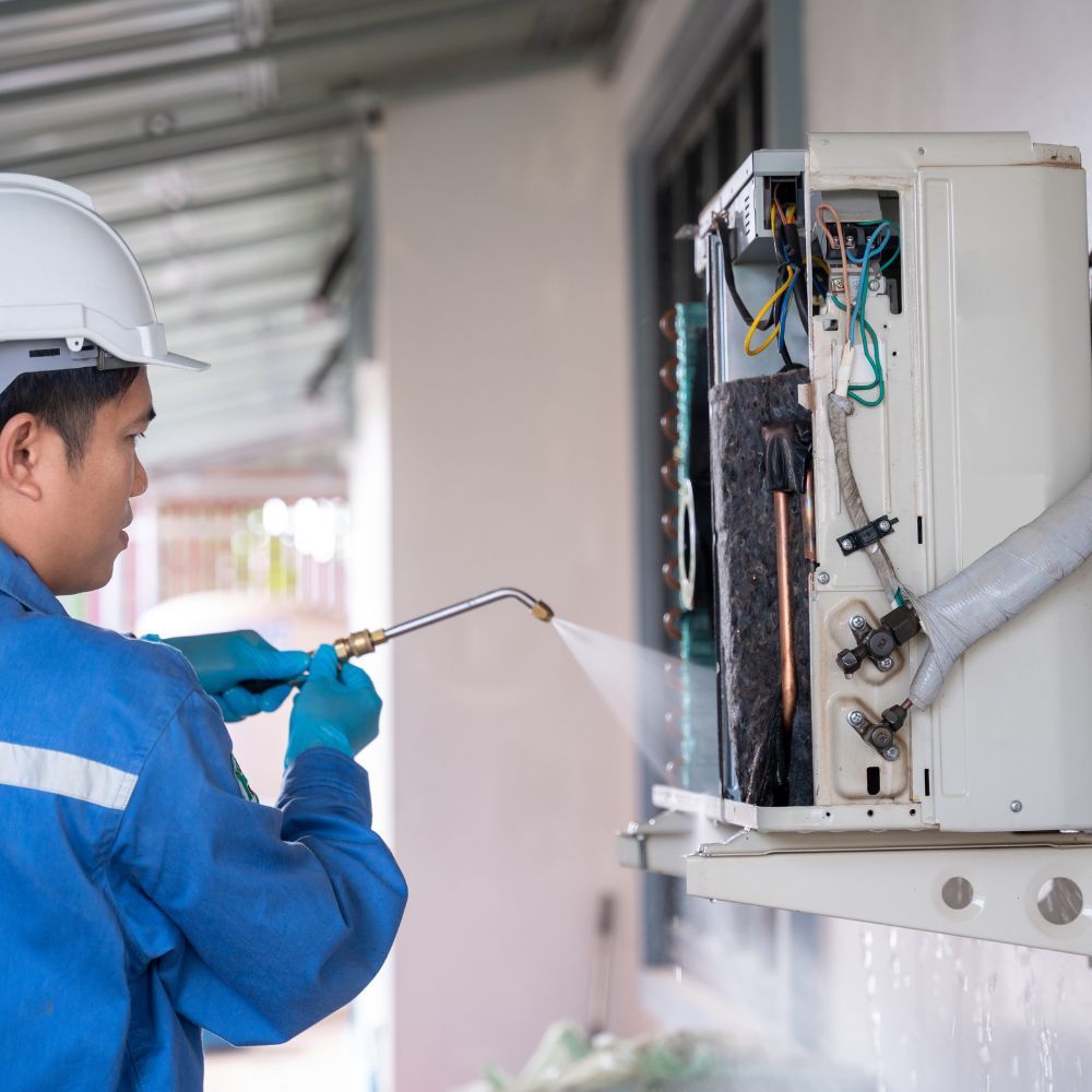 A man is spraying water on an air conditioner.