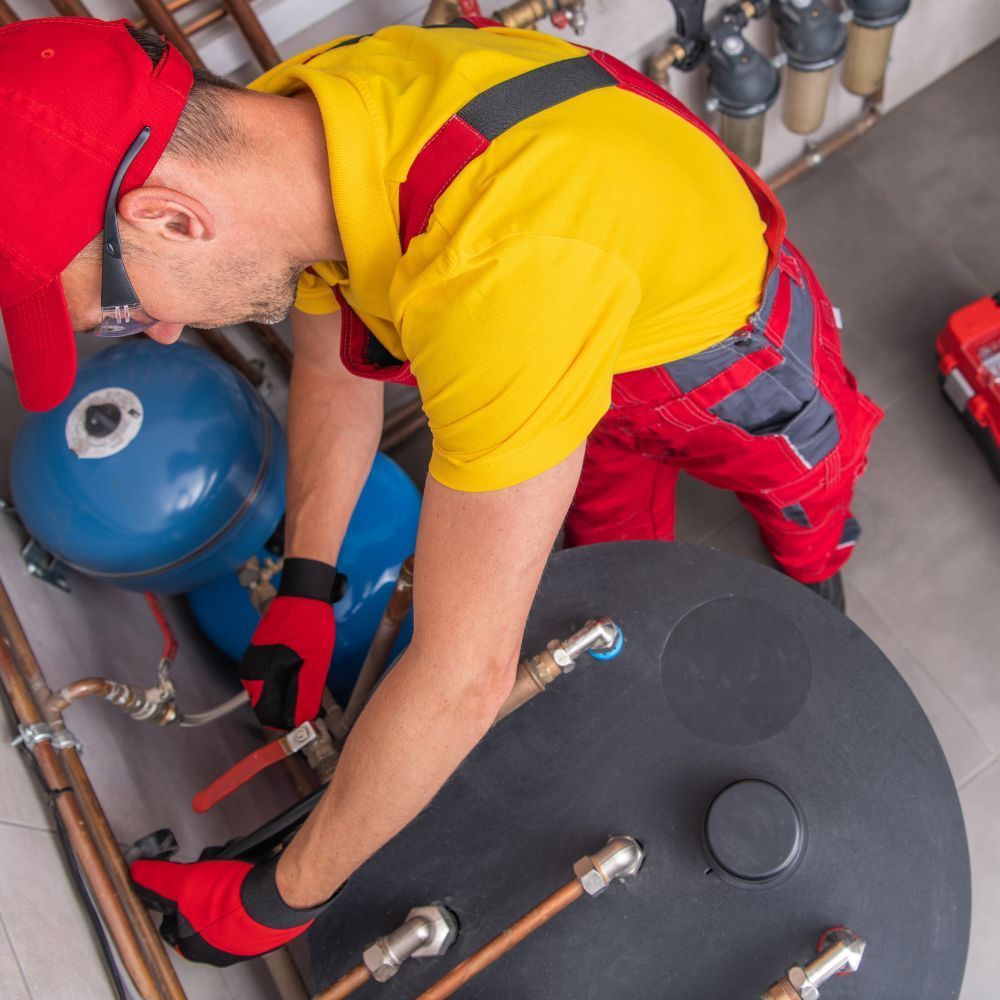 A man in a yellow shirt and red overalls is working on a water tank