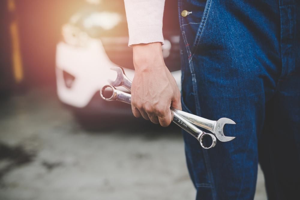 A Man Is Holding Two Wrenches In Front Of A Car — Reef Diesel Injection In North Mackay, QLD