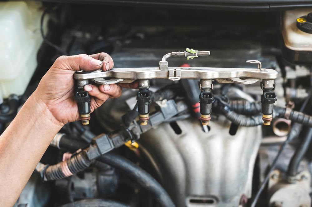 A Person Is Holding A Fuel Injector In Front Of A Car Engine — Reef Diesel Injection In Sarina, QLD