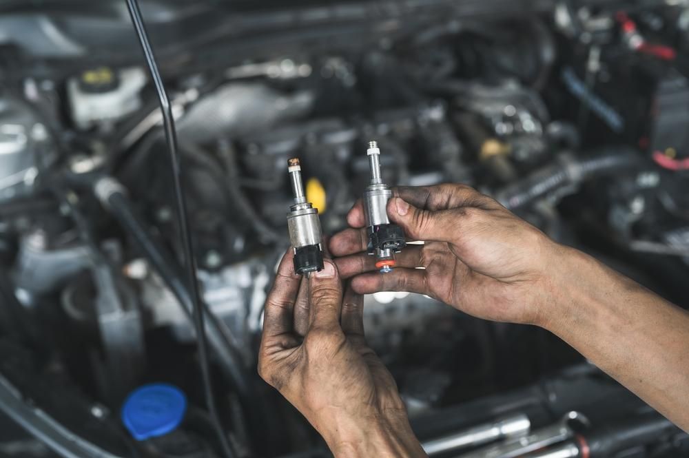 A Person Is Holding Two Fuel Injectors In Their Hands In Front Of A Car Engine — Reef Diesel Injection In Bowen Basin, QLD