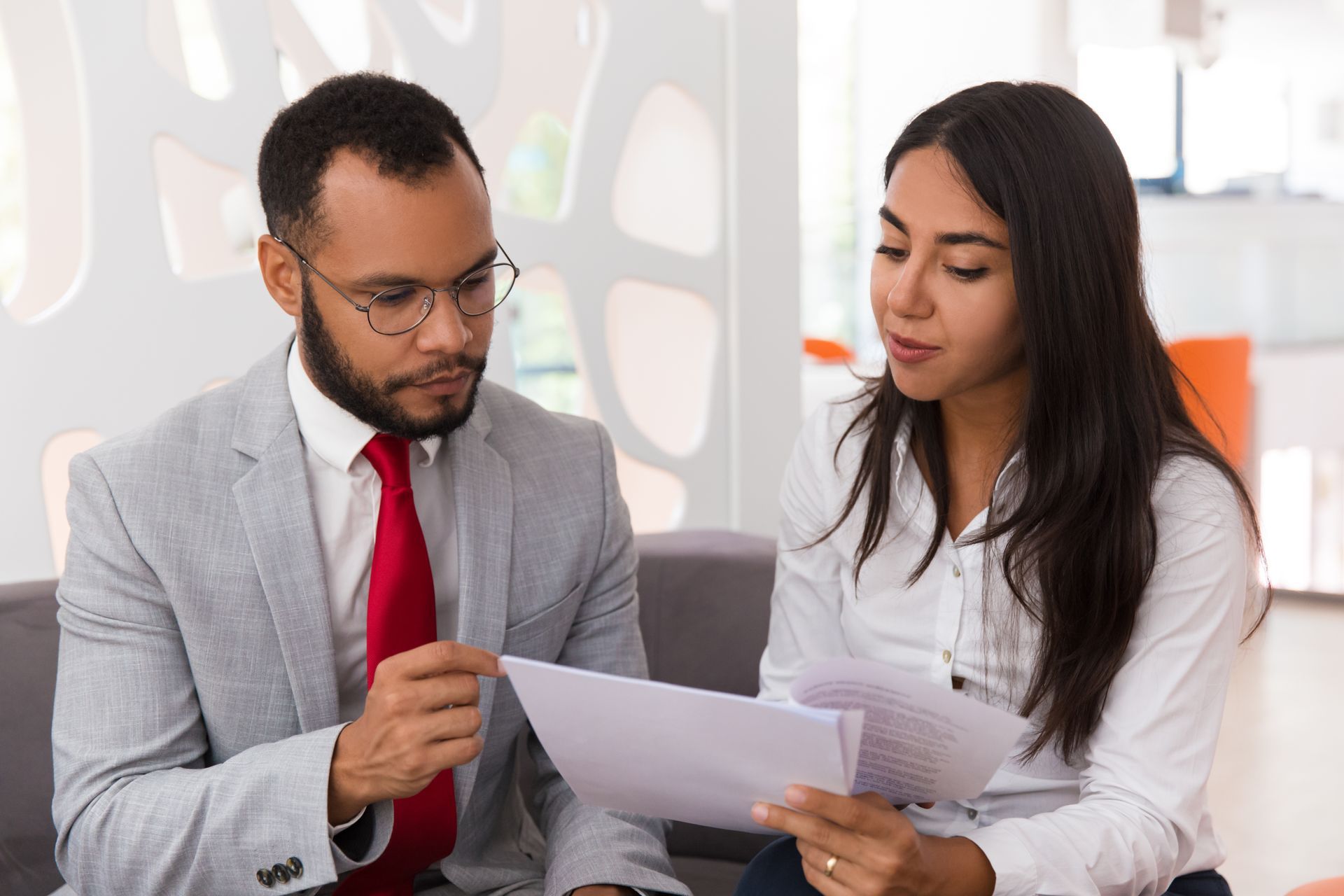 A man and a woman are sitting on a couch looking at a piece of paper.