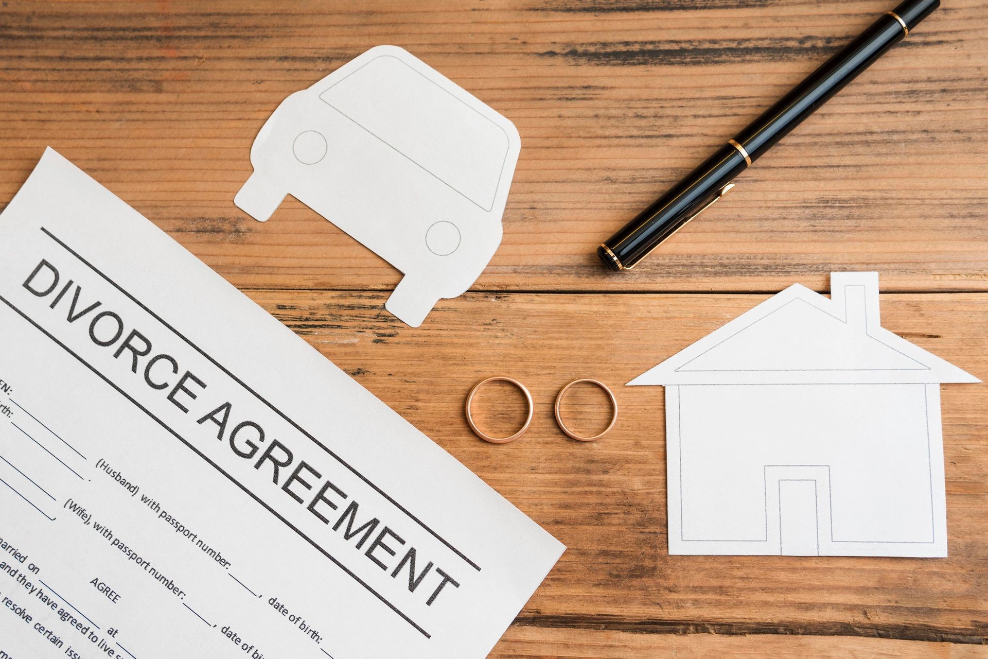 A divorce agreement is sitting on a wooden table next to a pen.