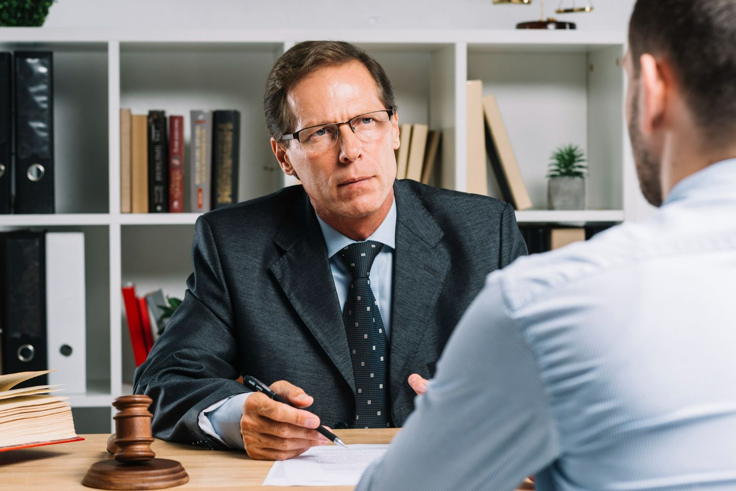 A man in a suit and tie is sitting at a desk talking to another man.