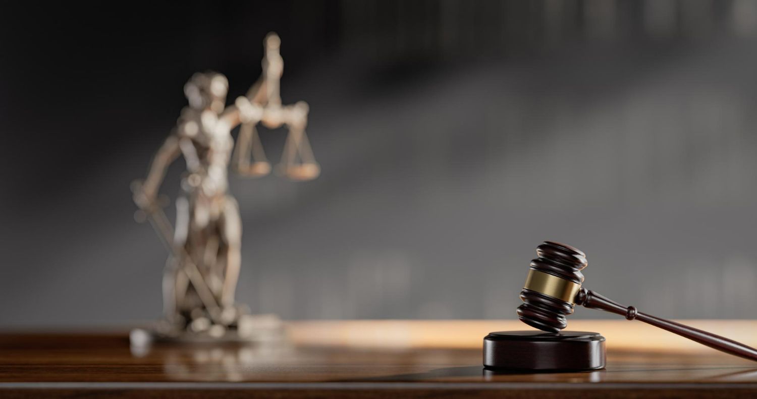 A statue of justice is sitting on a wooden table next to a judge 's gavel.