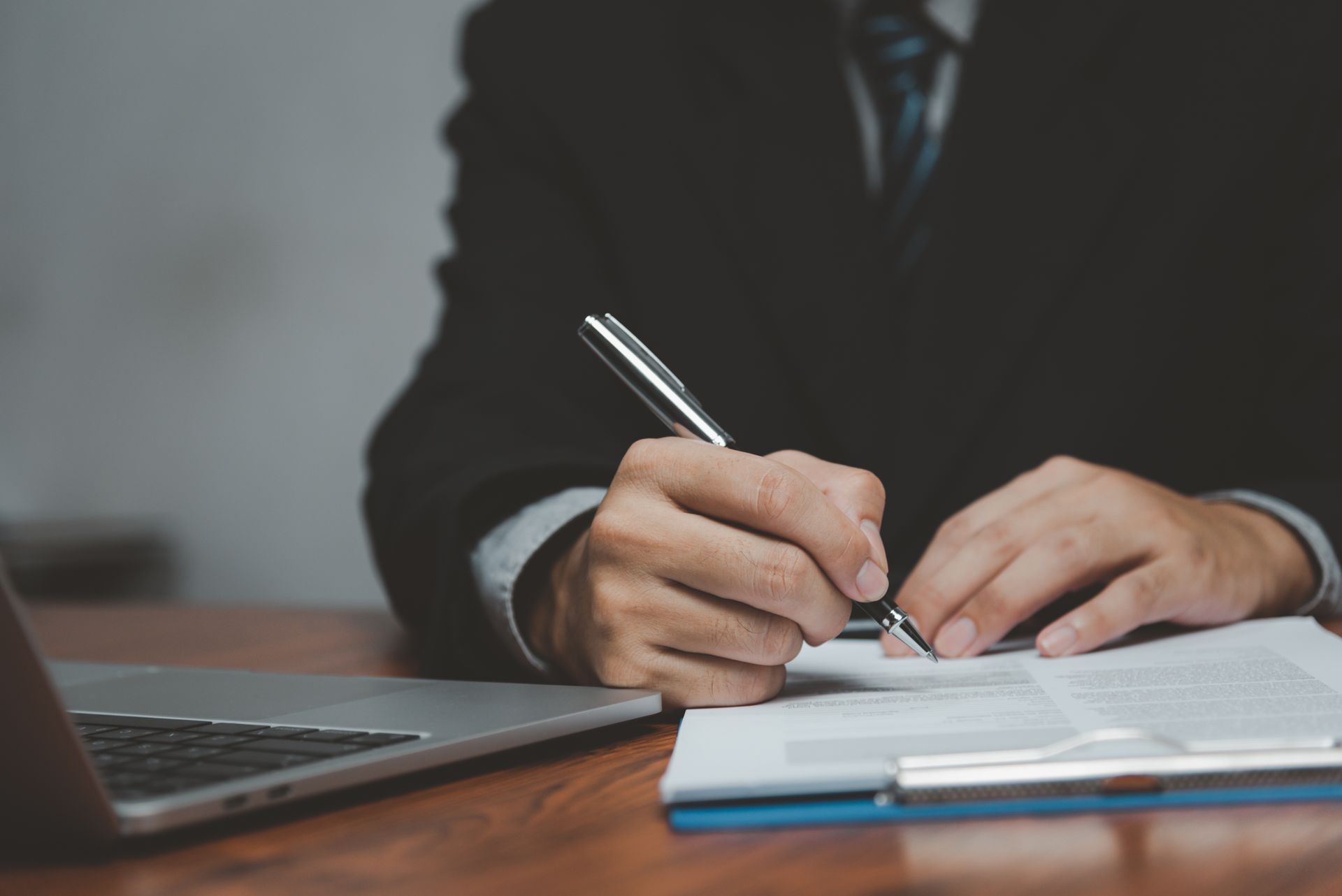 A man is sitting at a desk signing a document with a pen.