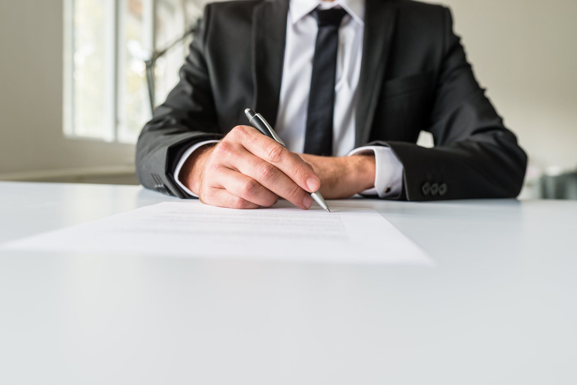 A man in a suit and tie is sitting at a table writing on a piece of paper.