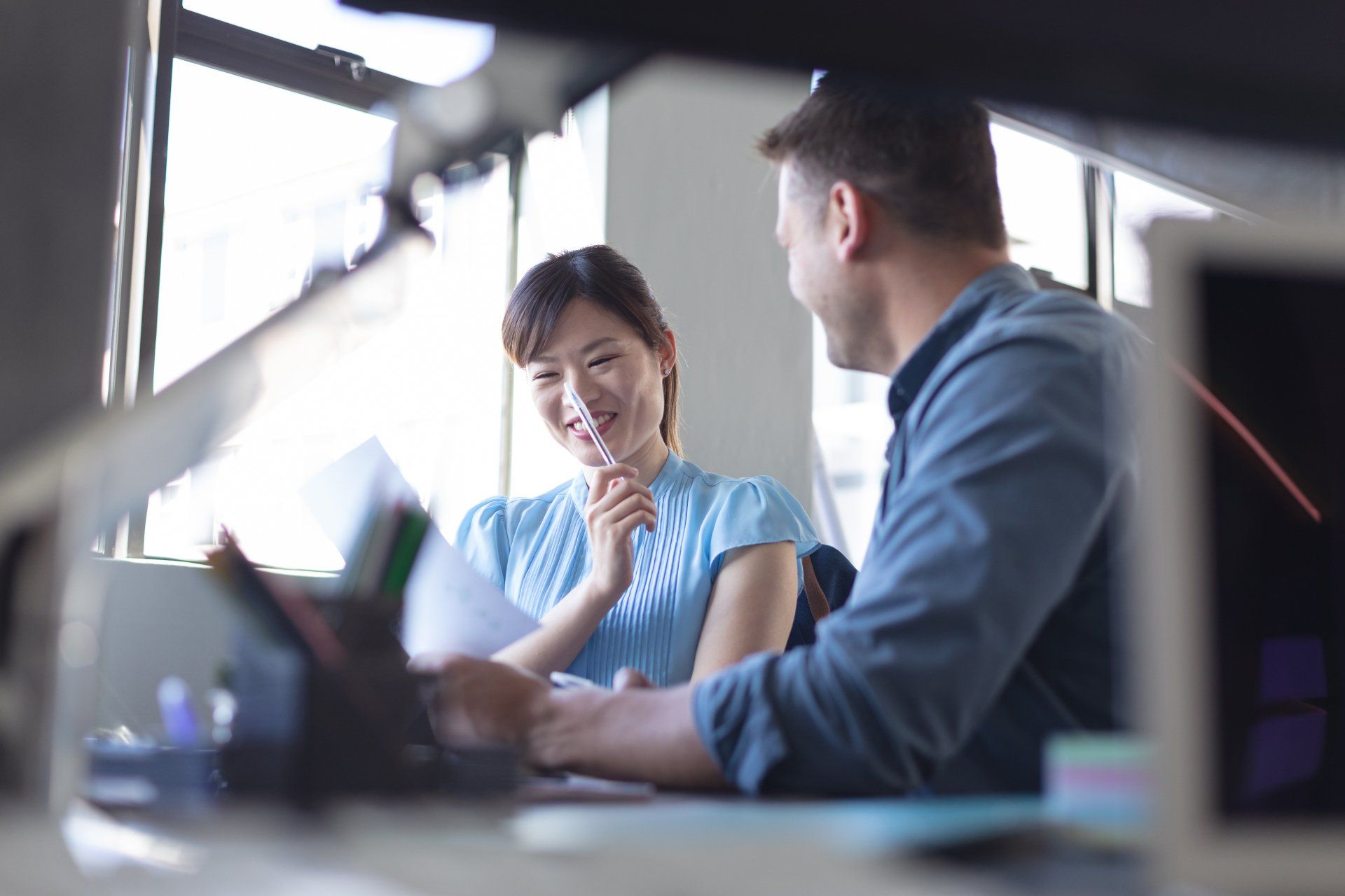 A man and a woman are sitting at a desk talking to each other.