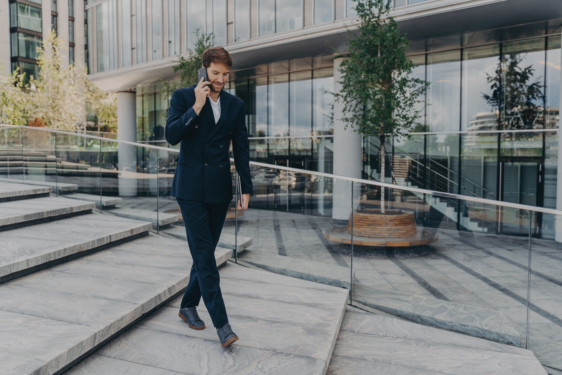 A man in a suit is walking down stairs while talking on a cell phone.