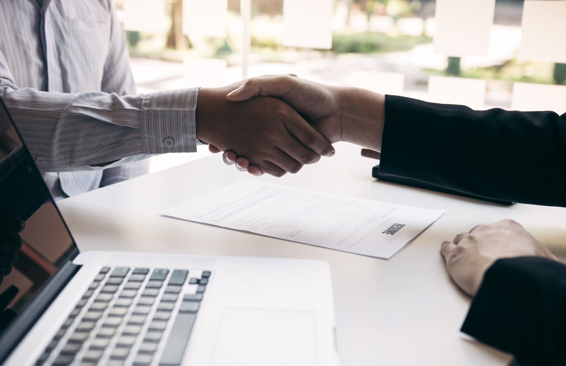 A man and a woman are shaking hands over a table with a laptop.
